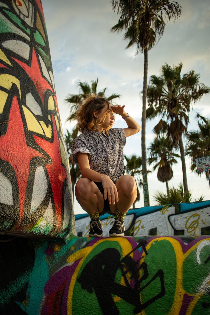 photo of woman squatting on graffiti wall posing while looking away